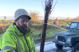 Laurence Maxwell working outside on winter day, holding tree sapling with Land Rover in the background